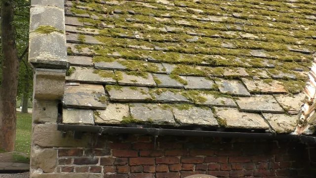 Old building mossy slate roof tilting down reveal millstone chained to red brick wall