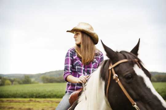 Cowgirl looking away while sitting on horse in field