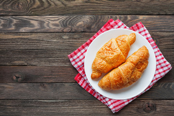 Continental breakfast background - pair of croissants on plaid red napkin. Rustic wooden background with place for text. Top view.