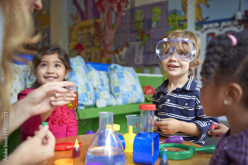 "Happy children doing science experiment at table in preschool" Stock