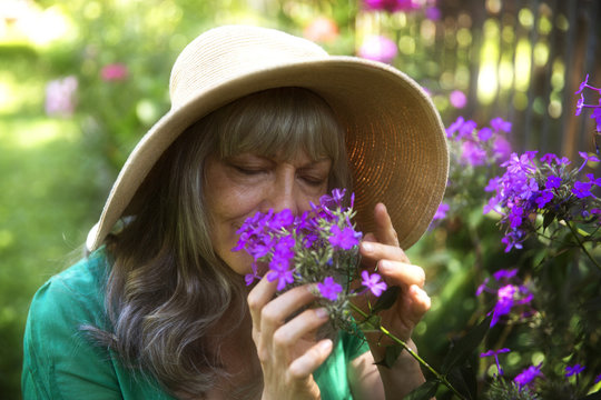 Senior woman with eyes closed smelling purple flowers in yard