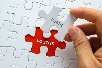 Hand holding piece of jigsaw puzzle with word PUBLIC POLICIES.