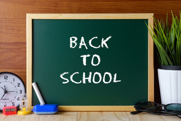 Words BACK TO SCHOOL written on green chalk board on wooden table.
