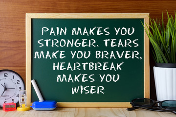 Word quote PAIN MAKES YOU STRONGER,TEARS MAKE YOU BRAVER,HEARTBREAK MAKES YOU WISER written on green chalk board on wooden table.