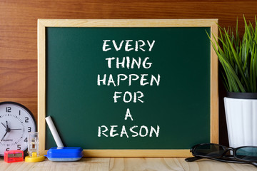 Word quote EVERY THING HAPPEN FOR A REASON written on green chalk board on wooden table.