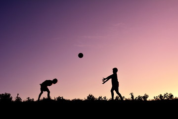 Silhouette children playing ball at sunset