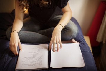 Low section of woman reading book on bed at home