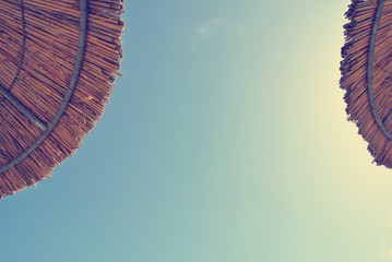 Low angle view on two straw parasols on the beach, on a sunny day, with blue sky in the middle. Can be used as summer background. Image filtered in faded, retro, Instagram style. Copy space. - 113207555