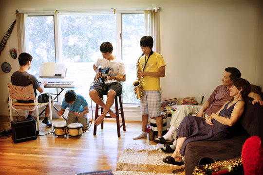 Parents looking at sons performing with music instruments in living room