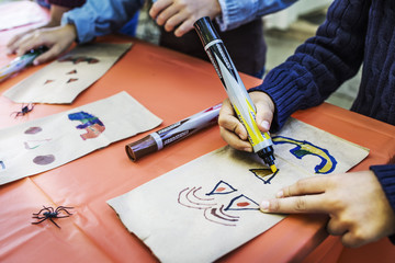 Cropped image of boy drawing on paper bags at table during Halloween party