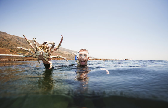 Portrait Of Excited Man Holding Large Crab While Swimming In Sea