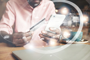 Visual effects. Worldwide connection interface. Cropped shot of African man, holding smart phone and credit card for making payments while shopping online, drinking cappuccino at a coffee shop