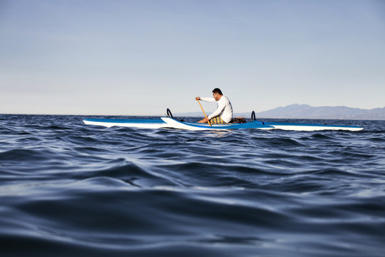 Man rowing outrigger on sea against clear sky