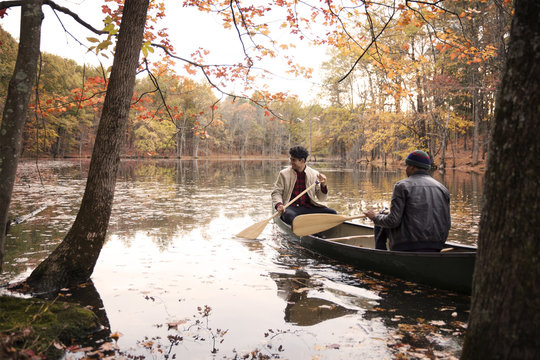 Friends Rowing Boat On Lake Amidst Trees At Forest