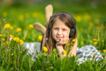 Little girl in headphones lying in the green grass.