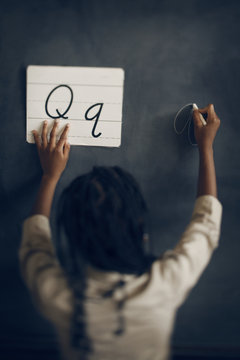 Rear view of schoolgirl writing letter Q on blackboard