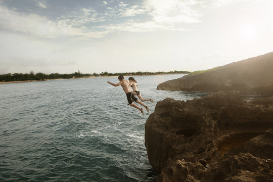 High Angle View Of Friends Diving In Sea From Cliff Against Sky