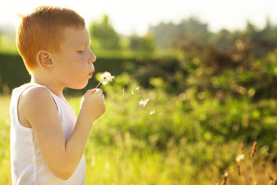 Side view of boy blowing dandelion while standing on field