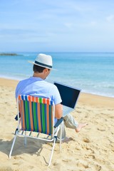 Business man using computer, tropical beach outdoors. Back view
