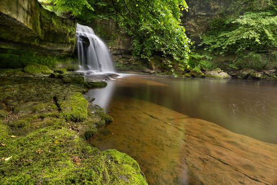 Fototapeta Remote woodland waterfall with green leaves in West Burton, North Yorkshire, UK.