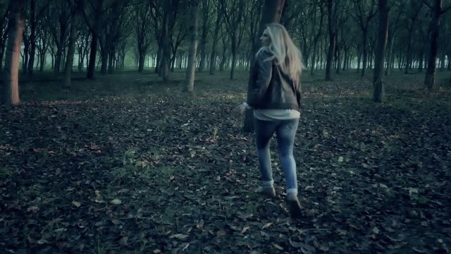 frightened afraid female woman runs away from murderer chasing her through a dark  forest full of trees looking for help horror scene