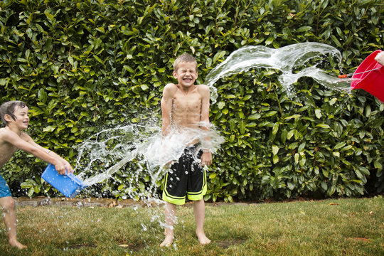 Water being splashed on shirtless boy at yard