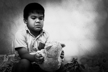 Kid pauper with old teddy bear sitting near the concrete wall,bl