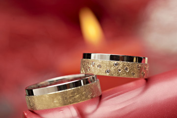 Close-up of two rings for wedding or engagement with red candle in background