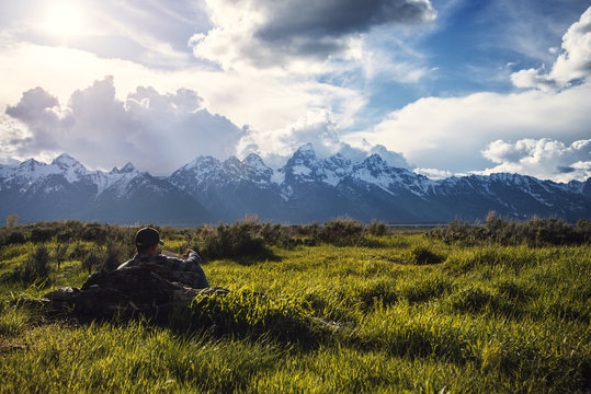 Man reading book while relaxing on grassy field against cloudy sky