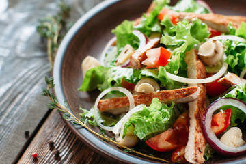 Chicken salad in clay plate on wooden background.Top view on clay brown plate with portion of chicken salad with mushrooms, onion and cumin seeds. Some free space for advertisement, blurred background