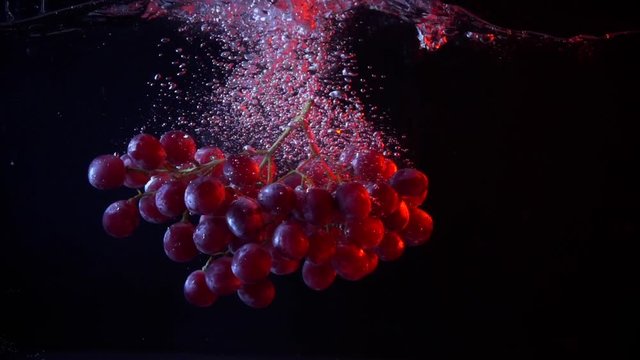 Red grapes fall into water with splashes super slow motion shot
