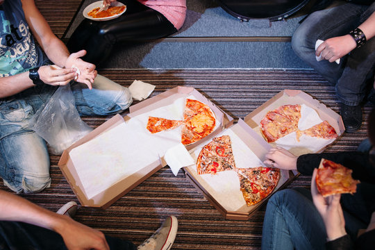 Having pizza snack on the floor. Top view on group of people eating pizza on the floor. Three boxes with pizza in the center of group.