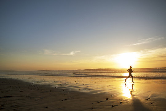 Silhouette of young man running along beach at sunset