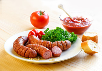 Roasted sausage with bread and vegetables served on white plate and wood board