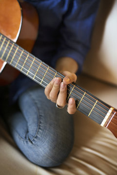 Cropped image of woman practicing guitar while sitting on sofa at home