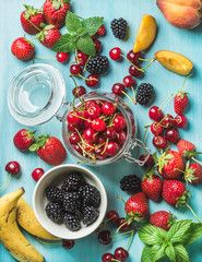 Healthy summer fruit variety. Sweet cherries, strawberries, blackberries, peaches, bananas and mint leaves on blue backdrop