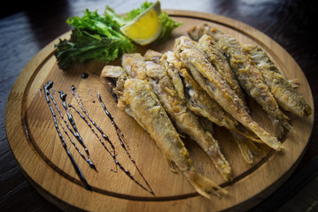 Fried red mullet fish on a wooden plate with lemon and salad