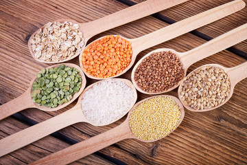 Groats in spoons on wooden table