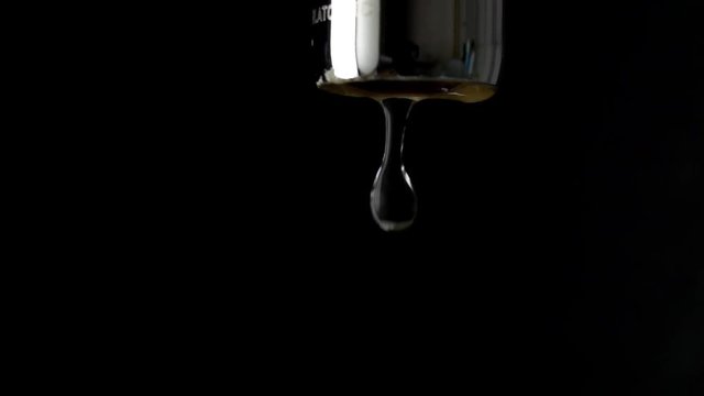 Macro slow motion shot of dripping chrome water tap against black background