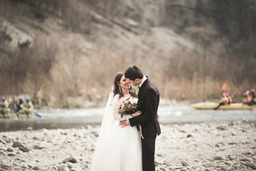 Beautifull wedding couple kissing and embracing near river with stones