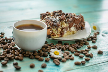 Cup of espresso, coffee beans, chamomile flower and cake on wooden turquoise table