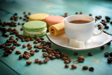 Cup of espresso, coffee beans, chamomile flower, cake, macaron (macaroon),waffles on wooden turquoise table.