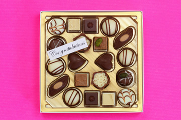 Congratulations card with box of assorted milky, white and pure chocolates on pink background
