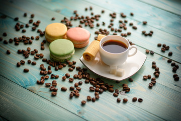 Cup of espresso, coffee beans, chamomile flower, cake, macaron (macaroon),waffles on wooden turquoise table.