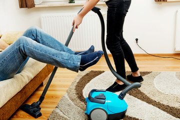 Woman vacuuming carpet man holding legs in the air