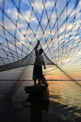 A fisherman casting a nets into the water during sunrise
