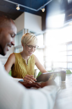 Two Creative Millenial Small Business Owners Working On Social Media Strategy Using A Digital Tablet While Sitting At Desk