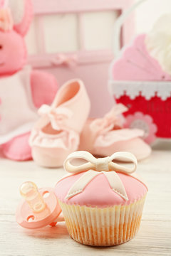 Tasty cupcake with bow and baby shoes, decorative baby carriage on color background