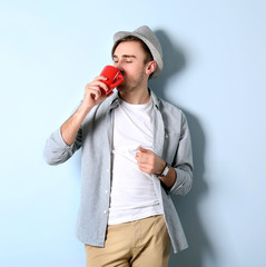 Young handsome man with a cup of coffee on light blue background