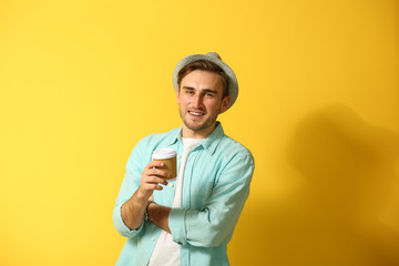 Young handsome man with a cup of coffee on bright yellow background